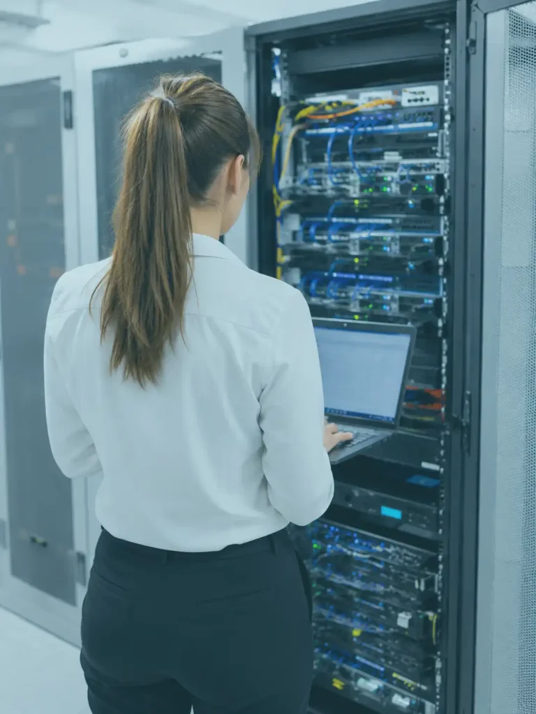 IT Mitarbeiterin arbeitet in einem modernen Serverraum an der Verwaltung und Überwachung der IT Infrastruktur. Die Aufnahme zeigt eine professionelle Arbeitsumgebung mit Servern, Netzwerktechnik und leistungsfähigen IT Systemen.